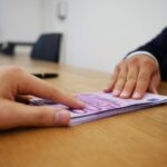 Persona anziana seduta su una sedia, con documenti e un computer portatile, in cerca di informazioni sull'assegno di accompagnamento.