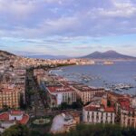 Panorama di Napoli con il Vesuvio sullo sfondo e il centro storico affollato di turisti.